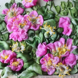 May include: Close-up of a pink and green ribbon embroidery of roses. The roses are made of pink satin ribbon and the leaves are made of green satin ribbon.