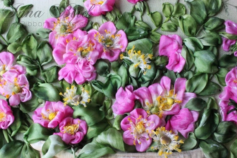 May include: Close-up of a pink and green ribbon embroidery of roses. The roses are made of pink satin ribbon and the leaves are made of green satin ribbon.