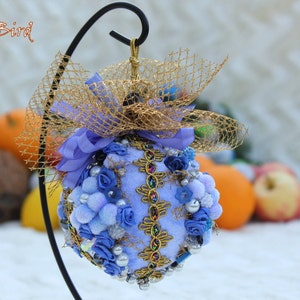 May include: A blue and gold Christmas bauble with a bow and a net. The bauble is decorated with blue flowers, beads, and sequins.