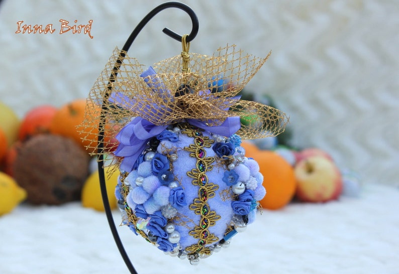 May include: A blue and gold Christmas bauble with a bow and a net. The bauble is decorated with blue flowers, beads, and sequins.