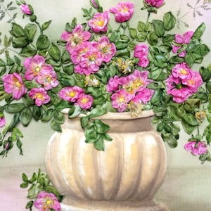 May include: A bouquet of pink silk ribbon roses in a cream-coloured ceramic vase with a ribbed design. The vase is sitting on a light green surface.