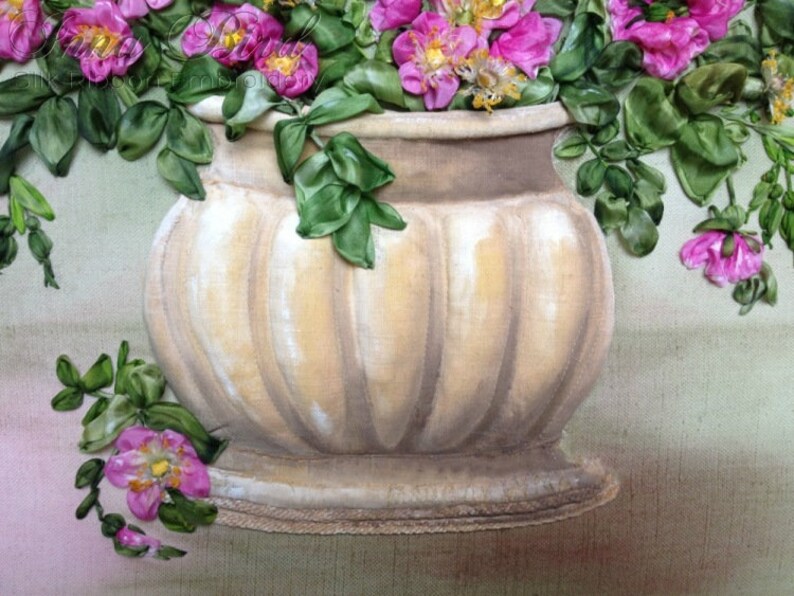 May include: A white ceramic vase with a ribbed design, filled with pink silk flowers and green leaves.