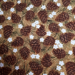 May include: A fabric pattern with a repeating design of brown pine cones, white flowers, and green pine needles on a tan background. The design has a natural, rustic aesthetic, suitable for various craft projects or home decor items.