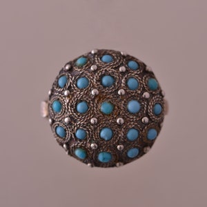 May include: A silver ring with a round turquoise stone setting. The stone is surrounded by a silver filigree design.
