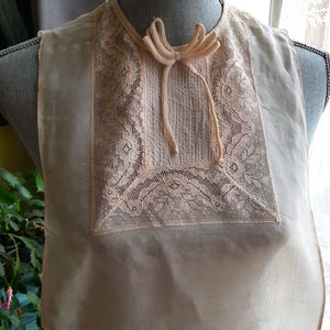 May include: A delicate, pale pink lace collar with a bow tie. The collar is made of a sheer fabric and has a delicate floral pattern.