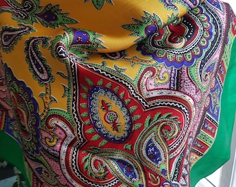 Può includere: Una vivace sciarpa quadrata con un motivo paisley. La sciarpa presenta uno sfondo giallo con disegni intricati in rosso, verde, blu e viola. Il bordo è verde unito. Questo accessorio è adatto a varie occasioni.