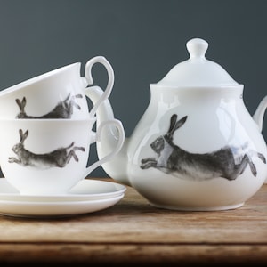 May include: A white teapot and three teacups with matching saucers. Each piece features a black and white illustration of a leaping hare.