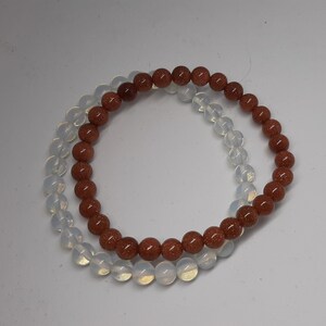 Peut inclure: Deux bracelets en perles, l'un avec des perles brunes et l'autre avec des perles blanches. Les bracelets sont superposés.