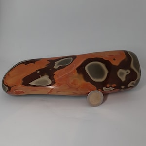 Op de afbeelding: Een grote, gladde, oranje, bruine en grijze steen met een uniek, swirlend patroon. De steen is ongeveer zo groot als een hand.