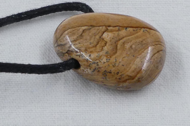Pode incluir: Um pingente de pedra marrom e bege com um cord&atilde;o preto. A pedra tem um padr&atilde;o de redemoinho e &eacute; lisa e polida.