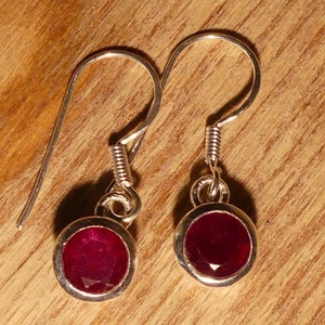 May include: A pair of silver earrings with red gemstone accents. The earrings have a simple, elegant design and are perfect for everyday wear.