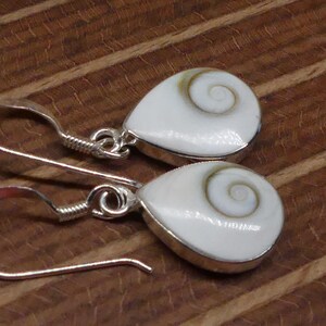 May include: A pair of silver earrings with white shell teardrop pendants featuring a brown spiral pattern.