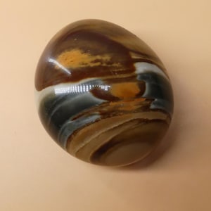 Op de afbeelding: Een gladde, gepolijste, eivormige steen met draaiende patronen in bruin, wit en grijs.