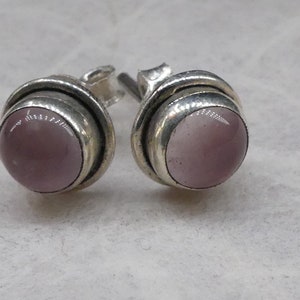 May include: A pair of silver stud earrings with pink gemstone accents.