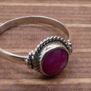 May include: A silver ring with a pink gemstone set in a twisted silver band.