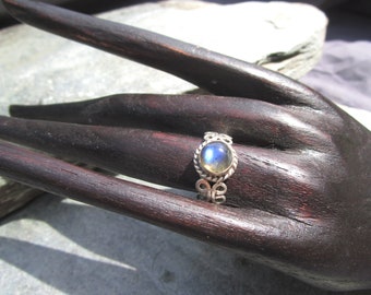 Op de afbeelding: Een zilveren ring met een ronde, iriserende labradorit-edelsteen gezet in een decoratieve, gedraaide band.