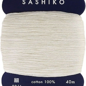 May include: A spool of white cotton thread labeled "Sashiko" with the text "cotton 100%", "20/4", "40m", and "daruma-ito.co.jp" on the label. The label also says "Made in Japan".