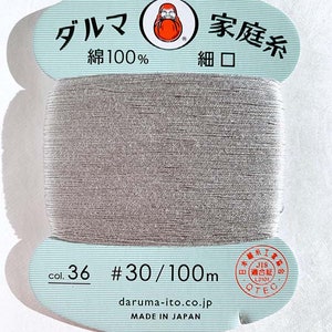 May include: A spool of gray Daruma brand cotton thread. The label is light blue with Japanese text and a Daruma doll logo. The spool is labeled with "col. 36 #30/100m" and "MADE IN JAPAN".
