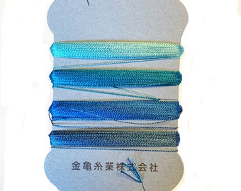 May include: A spool of blue and teal embroidery floss. The floss is wound on a gray cardboard spool with Japanese text. The colors range from light teal to deep blue. The floss is tightly wound and appears to be of high quality.