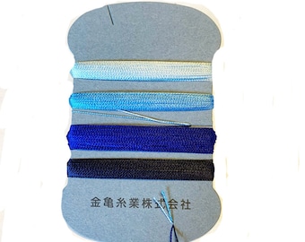May include: A spool of blue and white cords in varying shades of blue, from light to dark. The cords are neatly arranged on a gray cardboard backing with Japanese text.