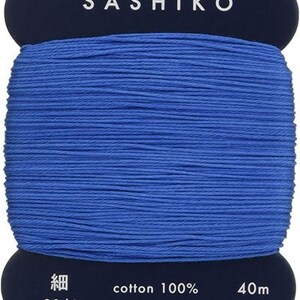 May include: A spool of blue cotton thread labeled "SASHIKO" with the text "cotton 100%", "20/4", "40m", and "daruma-ito.co.jp" on the label. The label also includes the text "MADE IN JAPAN".