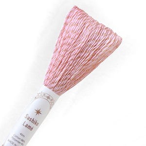May include: A skein of light pink Sashiko Lamé embroidery thread featuring metallic gold accents woven throughout the fibers. The paper label displays the text Sashiko Lamé, 40m, Cotton 96%, Polyester 4%, and includes a star graphic design.