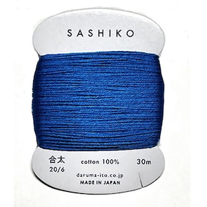 May include: A spool of blue Sashiko thread, a type of Japanese embroidery thread, made of 100% cotton. The label reads "Sashiko", "cotton 100%", "30m", "daruma-ito.co.jp", and "Made in Japan".
