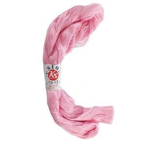 May include: A skein of light pink embroidery floss, with a white and blue label wrapped around the center. The label has Japanese text and a red and gold emblem. The floss is made of 100% cotton.