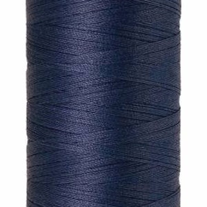 May include: A spool of navy blue Mettler Silk-Finish cotton thread. The spool has a lavender-colored top and bottom with the brand name and thread details printed on it. The thread is No. 50 and contains 500m/547yds of thread.