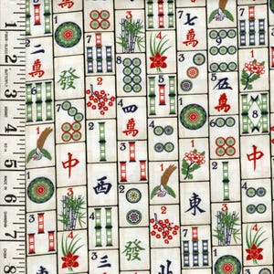 May include: A fabric featuring a repeating pattern of Mahjong tiles. The tiles are off-white with red, green, and black symbols and characters. A measuring tape is visible along the left side, marked in inches.