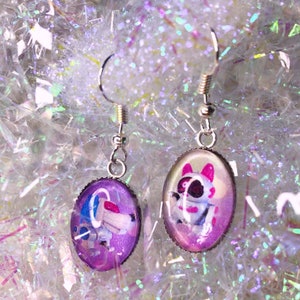 May include: A pair of silver earrings with purple and white glass cabochons featuring cartoon animal illustrations.