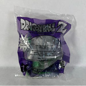 May include: A sealed plastic bag with a purple and green Dragon Ball Z logo. The bag contains a toy, with text that reads "THIS BAG IS NOT A TOY. Please discard." and "Made in China."