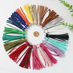 Puede incluir: Surtido de 20 borlas de cuero de colores vivos con anillos de metal plateado. Las borlas están dispuestas en círculo, con los anillos hacia afuera.