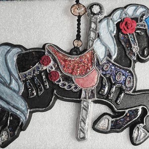 May include: A black carousel horse ornament with a red and pink saddle, adorned with red roses and sparkling accents. The horse has a silver mane and tail, with a blue accent on its head. A decorative piece for a festive occasion.