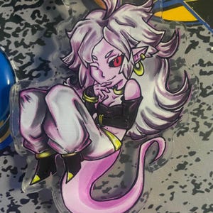 May include: A clear acrylic charm depicting a cartoon character with white hair, red eyes, and a pink tail. The character wears a black top and white trousers. The charm has a gold-coloured keyring.