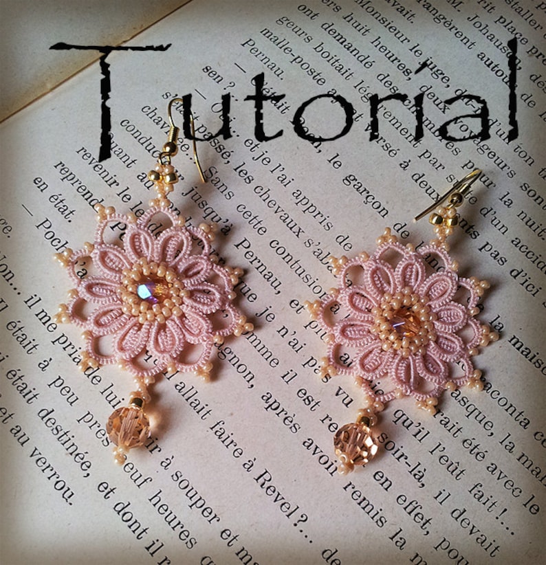 Pode incluir: Um par de delicados brincos de croch&ecirc; rosa com detalhes dourados. Os brincos t&ecirc;m a forma de flores com um pequeno cristal no centro de cada flor. Os brincos est&atilde;o pendurados em um livro com a palavra "Tutorial" escrita nele.