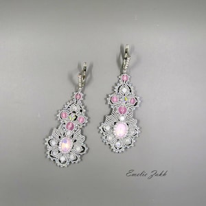 May include: A pair of silver earrings with pink and white stones. The earrings are made of delicate wirework and have a floral design. The earrings are hanging from silver hooks.