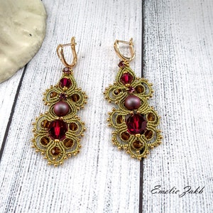 May include: Gold earrings with a burgundy and gold design. The earrings feature a pearl and red crystals.