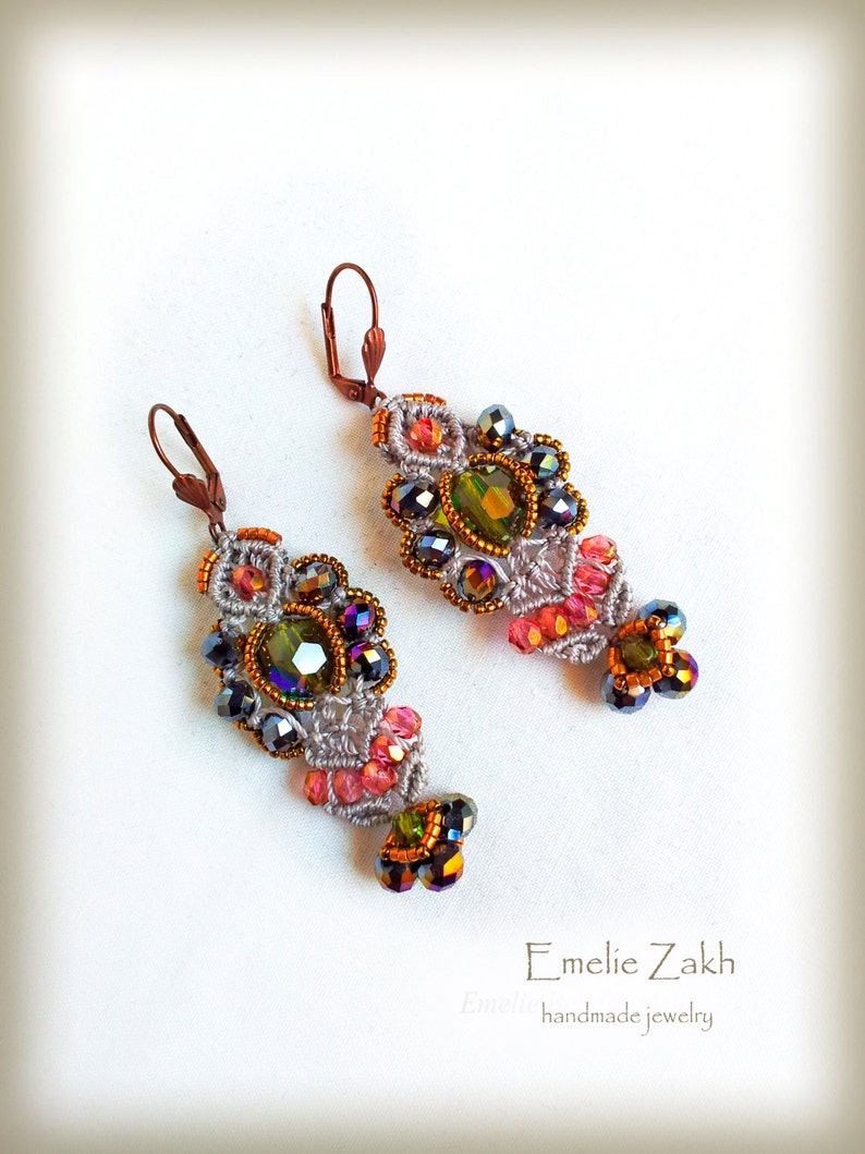May include: A pair of handmade earrings with a gray crocheted design, featuring pink, green, and black beads. The earrings have a unique, intricate design and are accented with iridescent crystals.