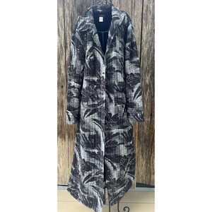 May include: A long, black and gray floral patterned coat. The coat has a notched collar, button closure, and a flowing silhouette. The floral pattern is a mix of dark and light shades, creating a textured look. The coat is displayed on a black metal hanger.