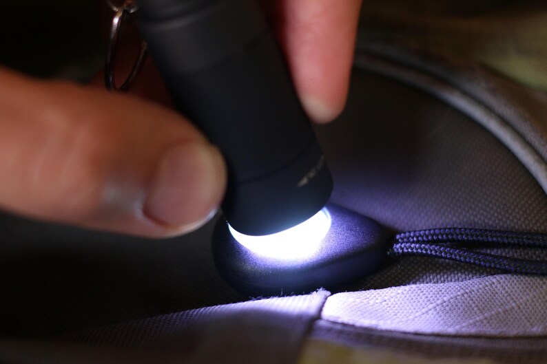 Op de afbeelding: Een zwarte zaklamp met een wit licht dat schijnt op een donkergrijs stofoppervlak.