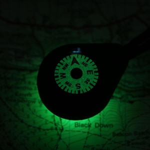 Op de afbeelding: Een groene, in het donker lichtgevende kompas met de letters N, S, E en W, en de richtingen NW, NE, SW en SE.