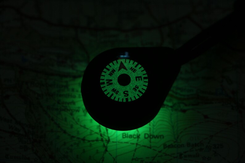 Op de afbeelding: Een groene, in het donker lichtgevende kompas met de letters N, S, E en W, en de richtingen NW, NE, SW en SE.