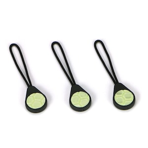 May include: Three black zipper pulls with a light green, textured, round,  football design.