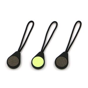 May include: Three black zipper pulls with black cords and oval grips. Two grips have a textured, grey surface, and one has a bright yellow-green surface. The pulls are arranged against a white background.