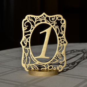 May include: Gold table number with a decorative floral design and the number "1" in the center.