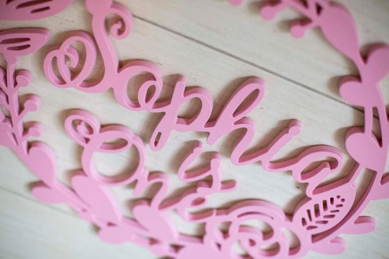 Puede incluir: Corte de madera rosa del nombre "Sophia" con la palabra "One" debajo, rodeado de un dise&ntilde;o floral.