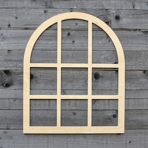 May include: A wooden arched window frame with nine square panes. The frame is light brown and is set against a gray wood background.