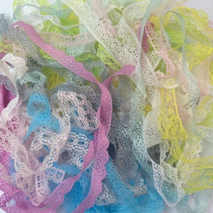 May include: A pile of colourful lace trim in various pastel shades, including pink, blue, yellow, and green. The lace is delicate and intricate, with a variety of patterns.