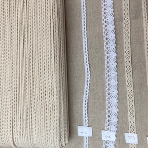 May include: Four different types of white cotton lace trim, labelled 1 through 4. The lace trim is displayed on a beige fabric background.